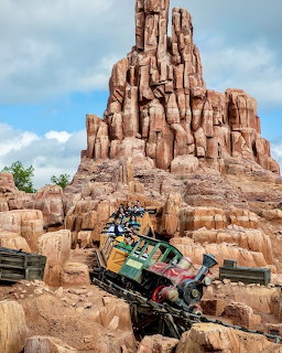 Roller coaster train ascending Big Thunder Mountain's red rock formation against blue sky