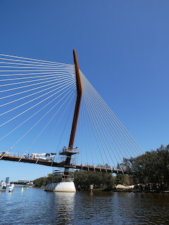 Cable-stayed bridge under construction with orange pylon and white cables over a river on a clear day