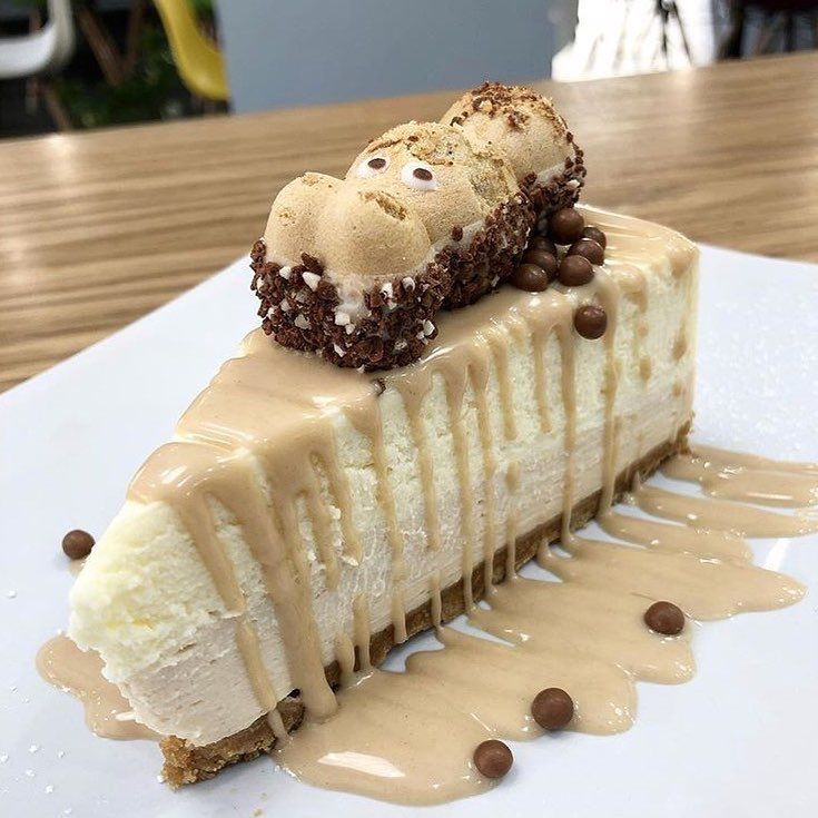 Slice of white cheesecake with Kinder chocolate topping and caramel drizzle on white plate