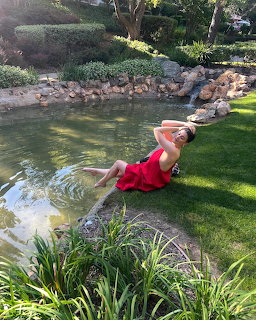 Woman in a red dress sitting beside a garden pond with her foot in the water