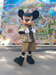 Mickey Mouse mascot in khaki safari costume posing before illustrated park map