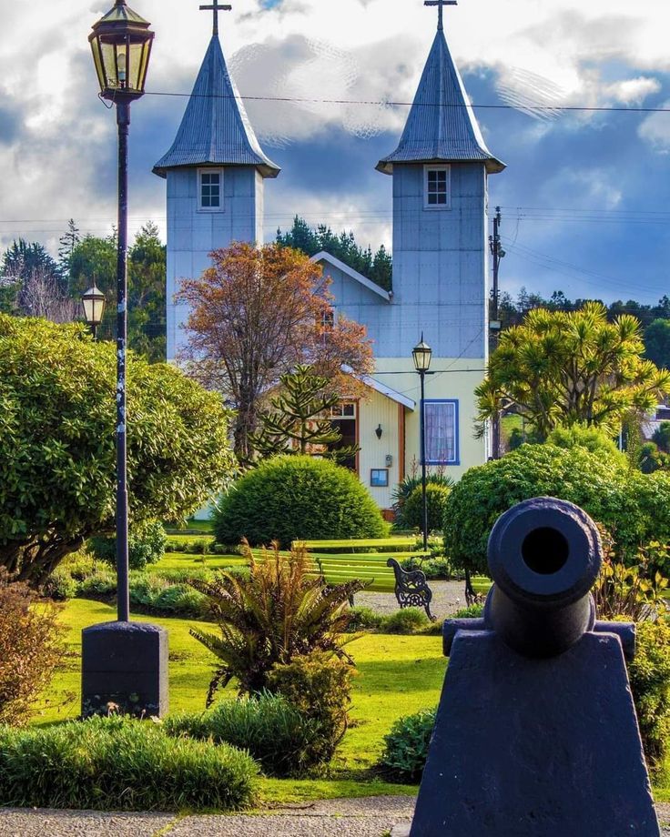 Twin-spired church behind a green plaza with cannon, lamp post, and gardens in Chacao, Chile