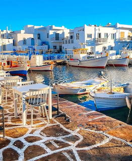 Colorful fishing boats in a Greek harbor with white buildings and cafe tables in the foreground