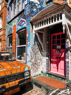 Colorful mosaic-covered building with red door and orange vintage truck parked outside