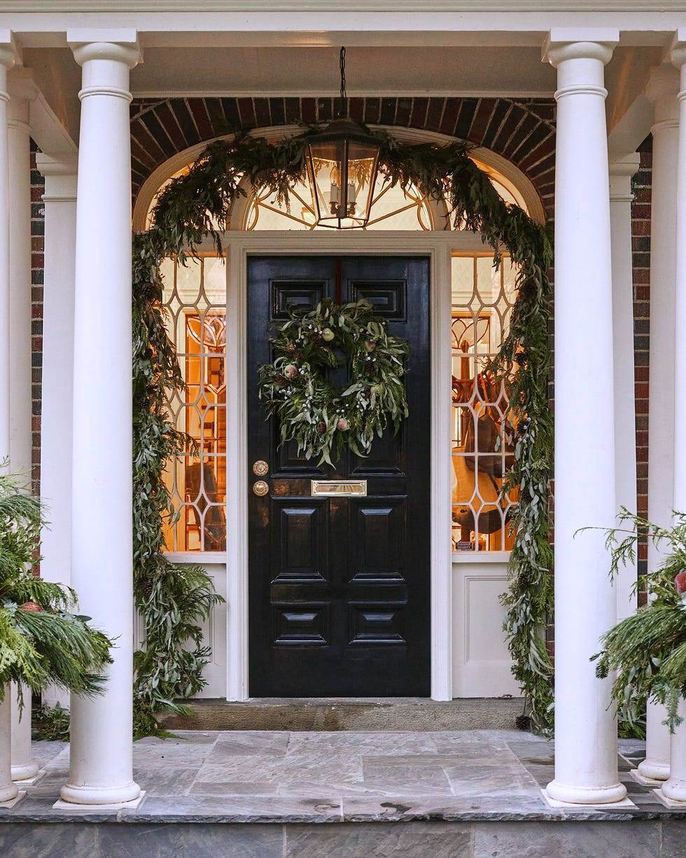 Colonial home entryway with white columns, black front door, wreath, and holiday garland greenery