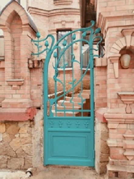 Turquoise wrought iron gate in a brick and stone doorway with steps behind