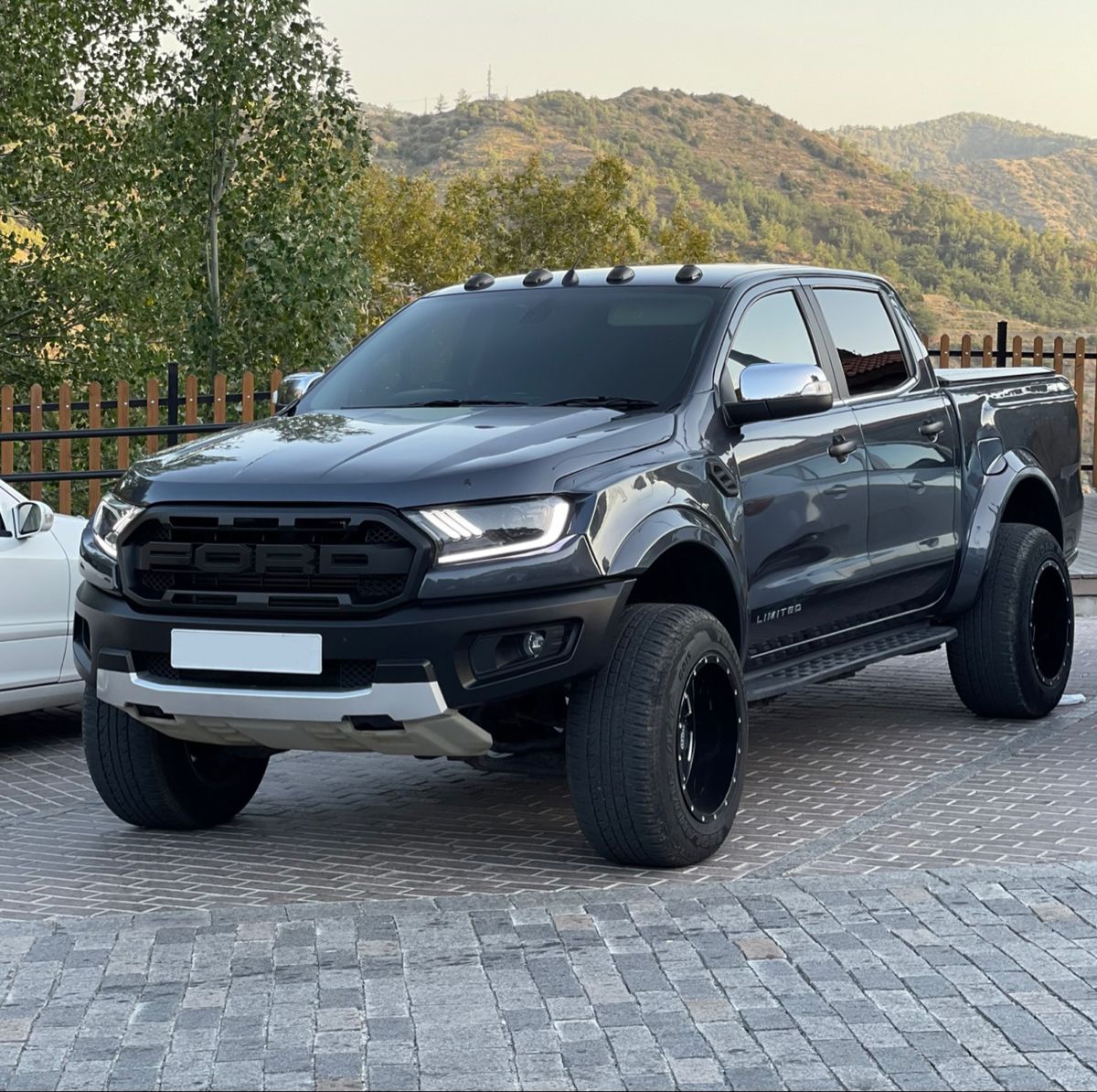 Black lifted pickup truck parked on a paved driveway with mountains behind