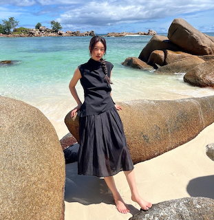 Woman in a black dress standing barefoot on a rocky tropical beach