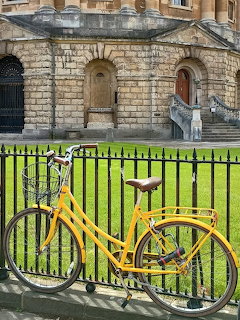 Yellow bicycle leaning against black iron railings in front of a stone historic building with arched doorway