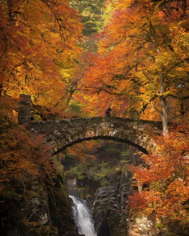 Stone bridge over waterfall in autumn forest with golden orange foliage