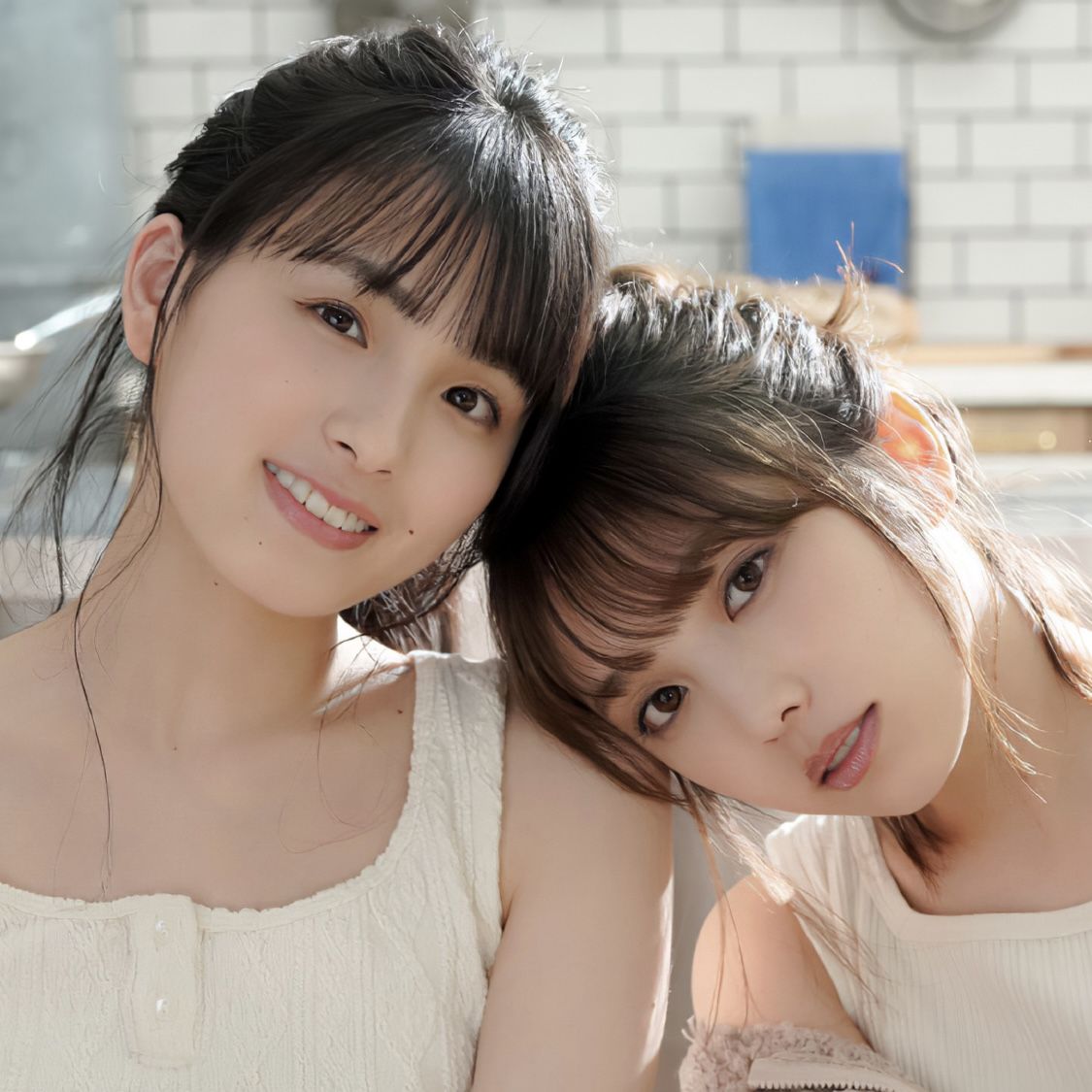Two young women in light tops posing closely together indoors