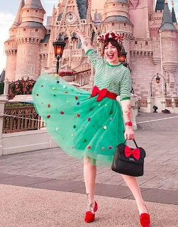 Woman in green outfit with red accessories standing before pink Disney castle
