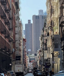 Narrow city street lined with buildings and fire escapes, skyscrapers visible in background