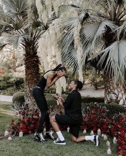 Person kneeling proposing marriage to partner outdoors with palm trees and flowers