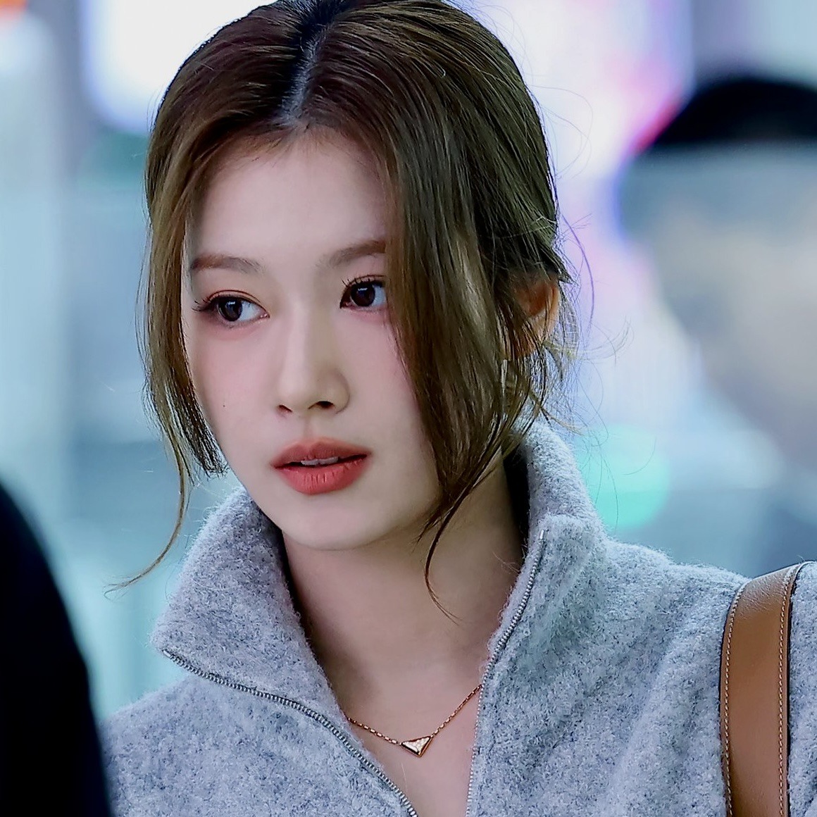 Close-up portrait of a young woman with tied-back hair in a gray jacket