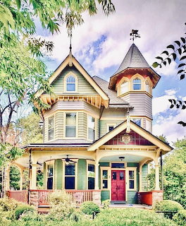 Colorful Victorian house with round turret, ornate gingerbread trim, and wrap-around porch in garden setting