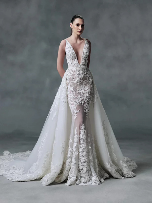 Model wearing a white lace wedding gown with deep V-neckline and detachable tulle overskirt