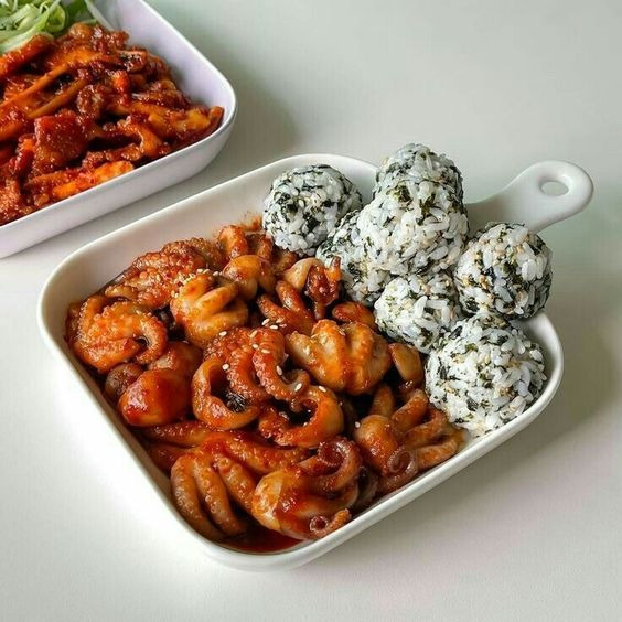 Spicy braised octopus with rice balls garnished with black sesame and seaweed on white serving plate