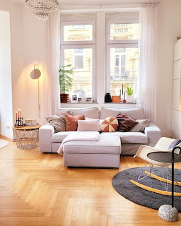 Cozy modern living room with gray sectional sofa, ottoman, herringbone parquet flooring, and tall windows