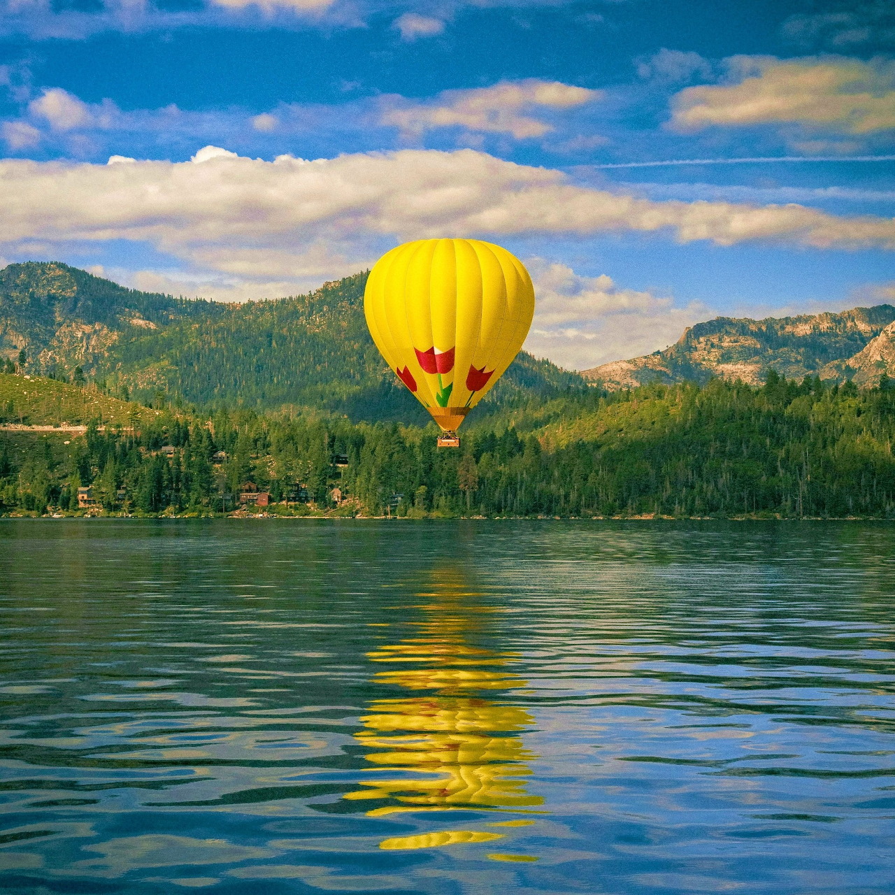 Yellow hot air balloon over a lake with mountain hills and its reflection in the water