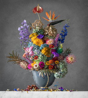 Elaborate colorful flower bouquet in blue vase on gray background with scattered petals