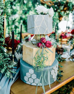 Three-tier wedding cake with gray tiers, gold accents, flowers, and greenery on a table
