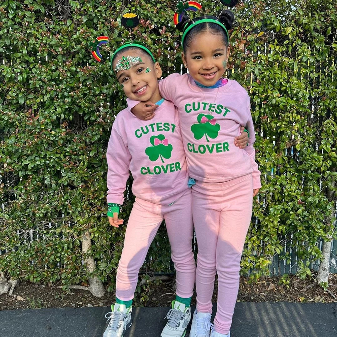 Two children wearing pink clover-themed sweatshirts standing together outdoors