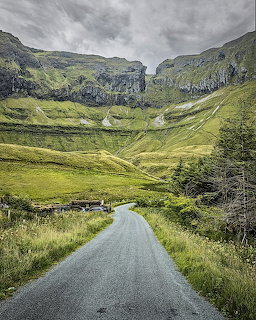 Country road leading into the green Gleniff Horseshoe valley under cloudy skies
