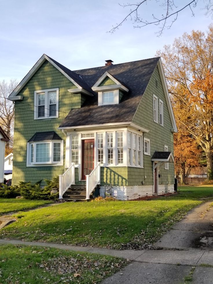 Green colonial house with white trim, covered porch, and dormer windows on an autumn day