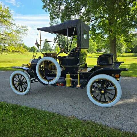 Black vintage Model T runabout car with white tires parked on green grass under trees