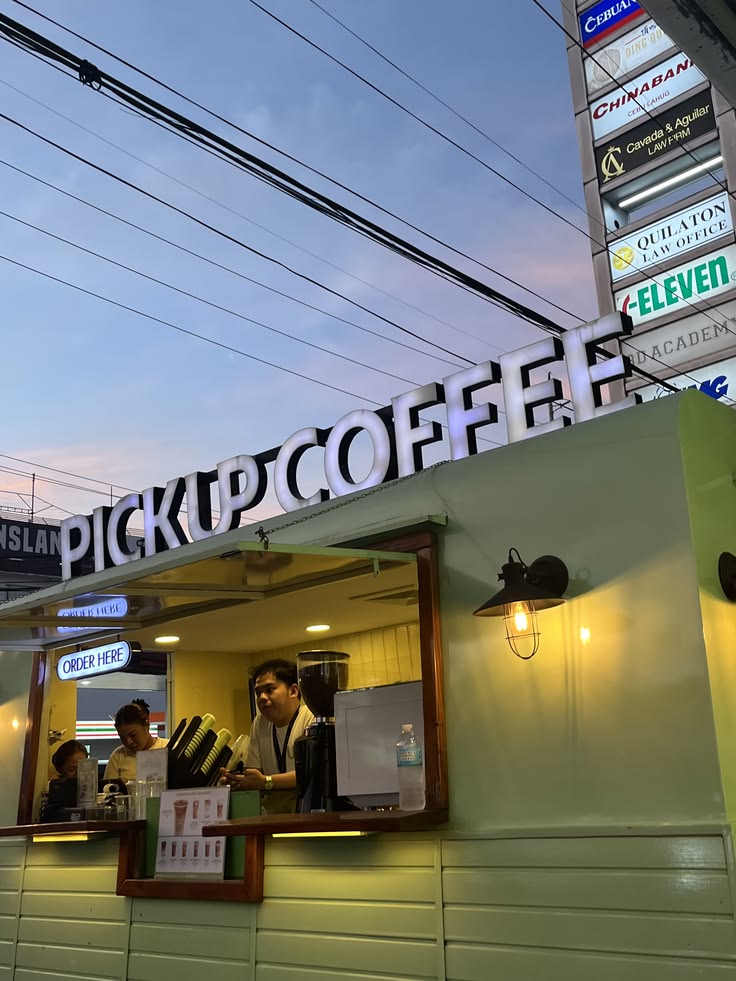 Pickup Coffee shop exterior at dusk with illuminated sign and staff at service window