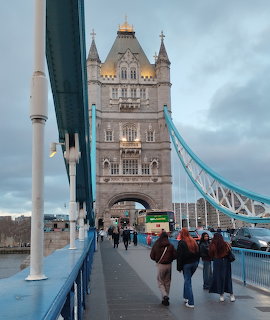People walking on Tower Bridge in London with Gothic towers and blue cables against cloudy sky