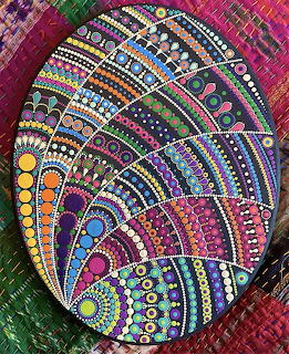 Colorful hand-painted egg with intricate mandala dot patterns in rainbow colors on patterned fabric