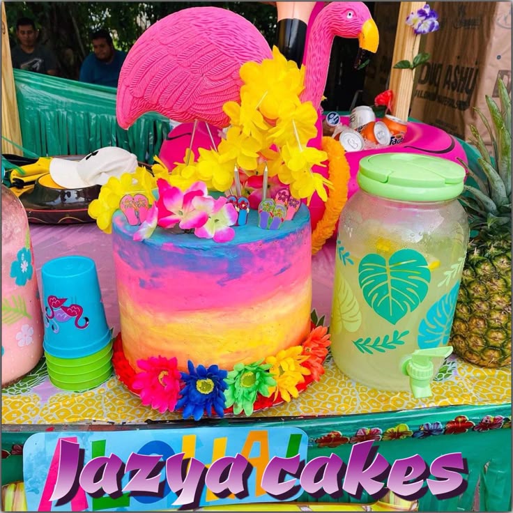 Bright flamingo-themed pastel cake with flowers next to a tropical drink jar