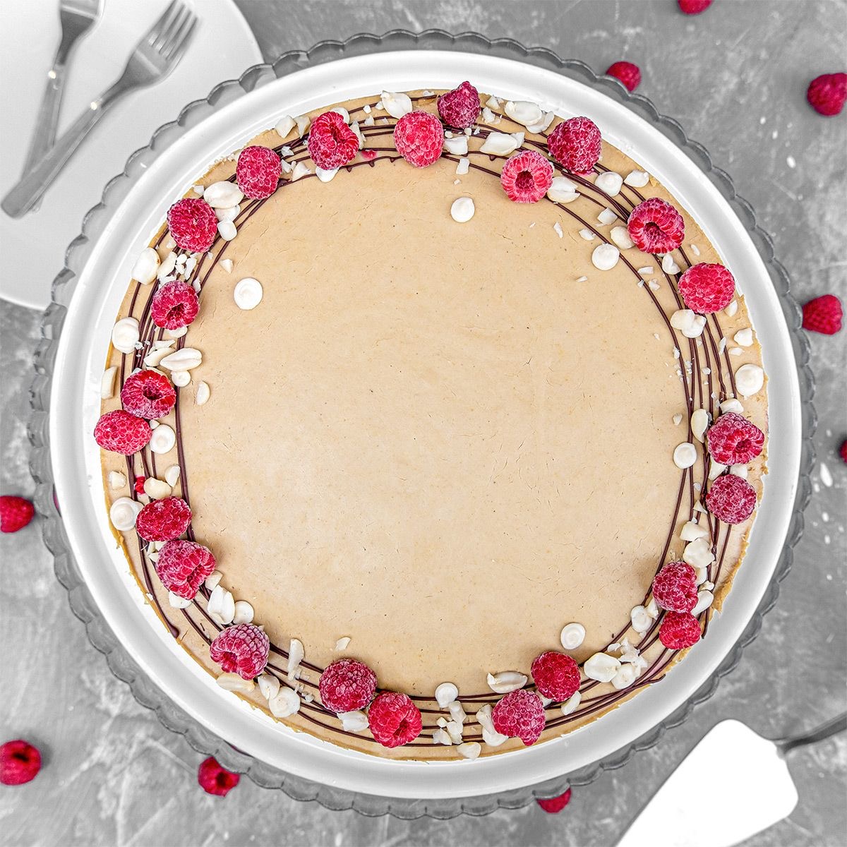 Top view of a round cake decorated with pink flowers, white meringues, and chocolate drizzle