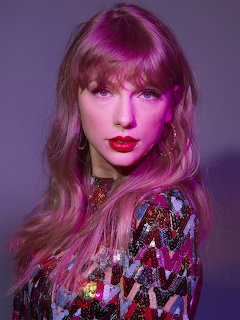 Woman with pink hair, bangs, red lipstick, and sequined top posing against a purple background