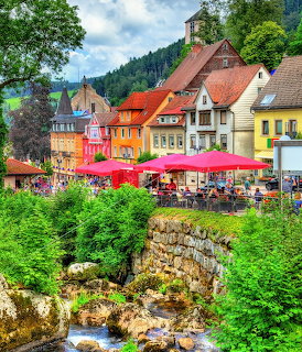 Colorful German village with half-timbered houses, red cafe umbrellas, greenery, and a stream
