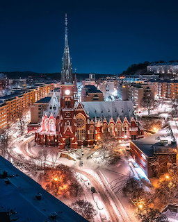 Gothic church with tall spire illuminated at night in a snow-covered city, aerial view