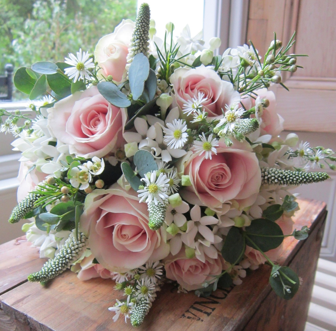 Pink rose and white daisy bouquet on a wooden windowsill beside a bright window