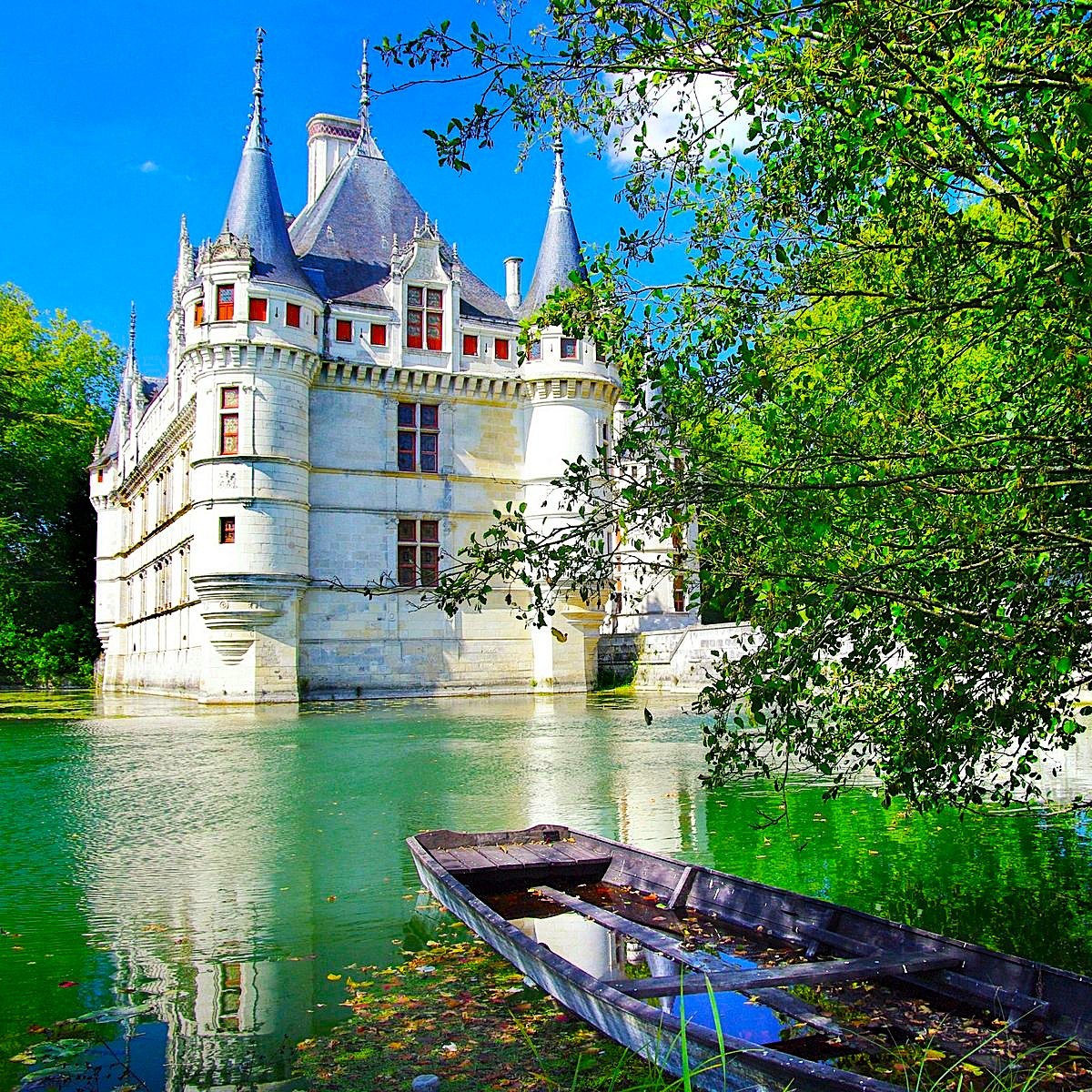 White French Renaissance castle with turrets on water moat, wooden boat, trees