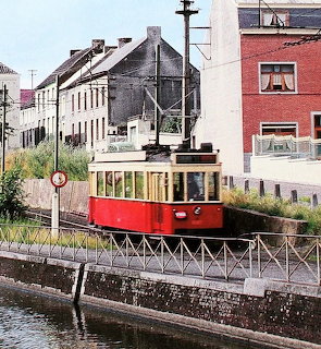 Red vintage tram on tracks beside a canal with city buildings behind it