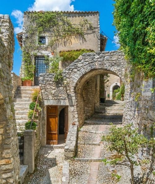 Cobblestone alley with stone arch gateway in a medieval village surrounded by greenery