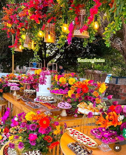 Festive outdoor table overflowing with bright pink, orange, yellow and purple flower arrangements in a garden setting