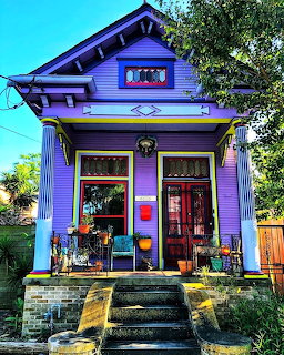 Purple Victorian house with ornate trim, front porch, and steps surrounded by trees