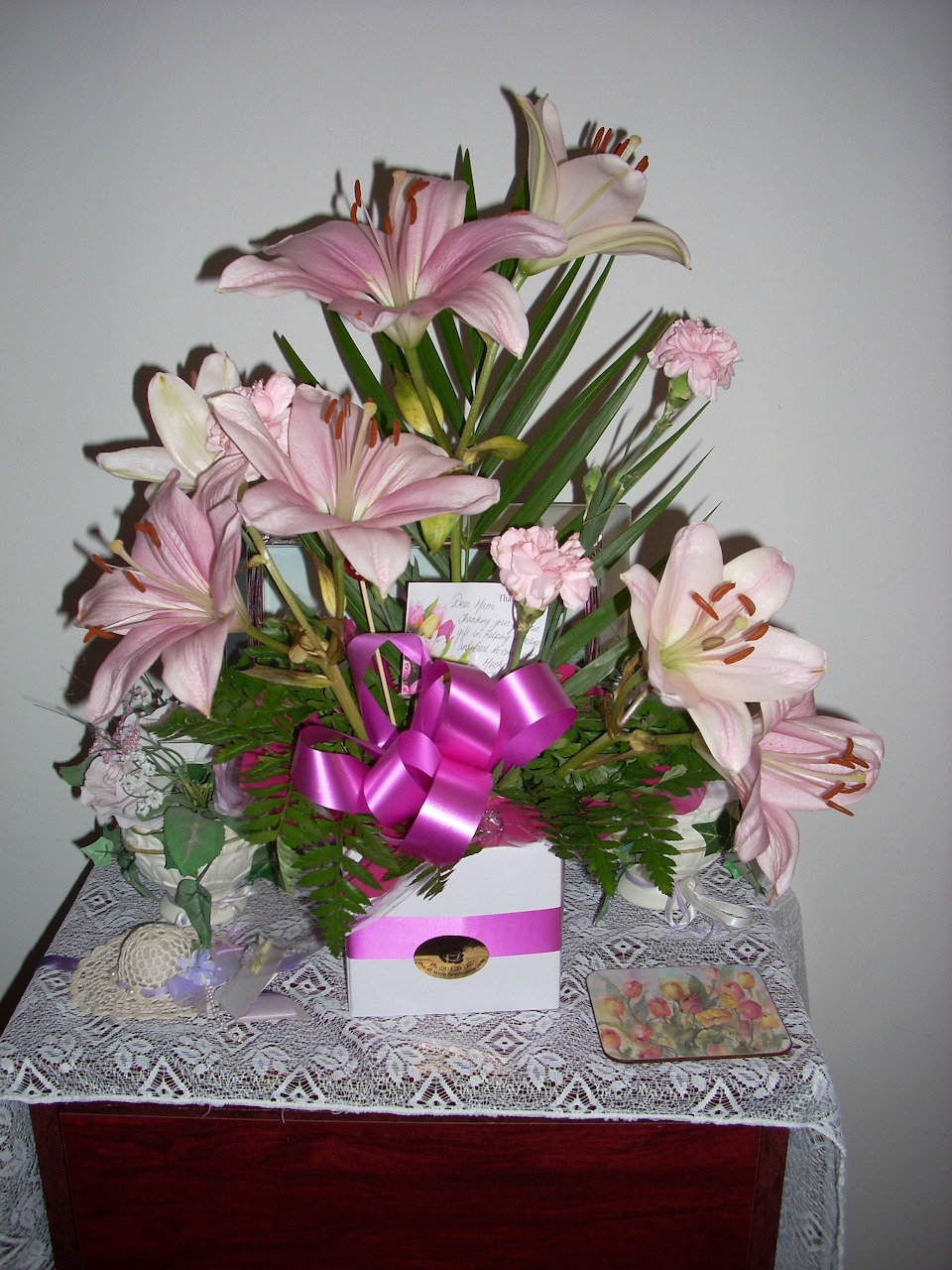 Pink lily and rose flower arrangement with magenta bow on lace tablecloth