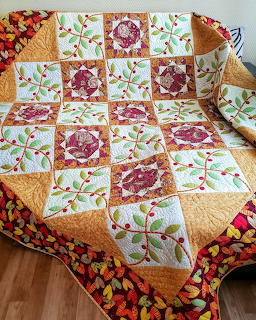 Patchwork quilt with red flowers, fall leaves, and golden squares on white background with floral border