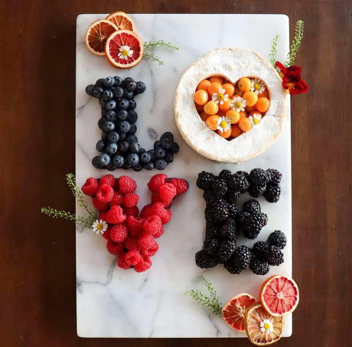 Fresh berries and fruit arranged spelling LOVE on white marble board with heart-shaped melon center