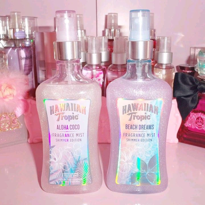 Two Hawaiian Tropic fragrance mist bottles on a pink vanity with perfume bottles behind them