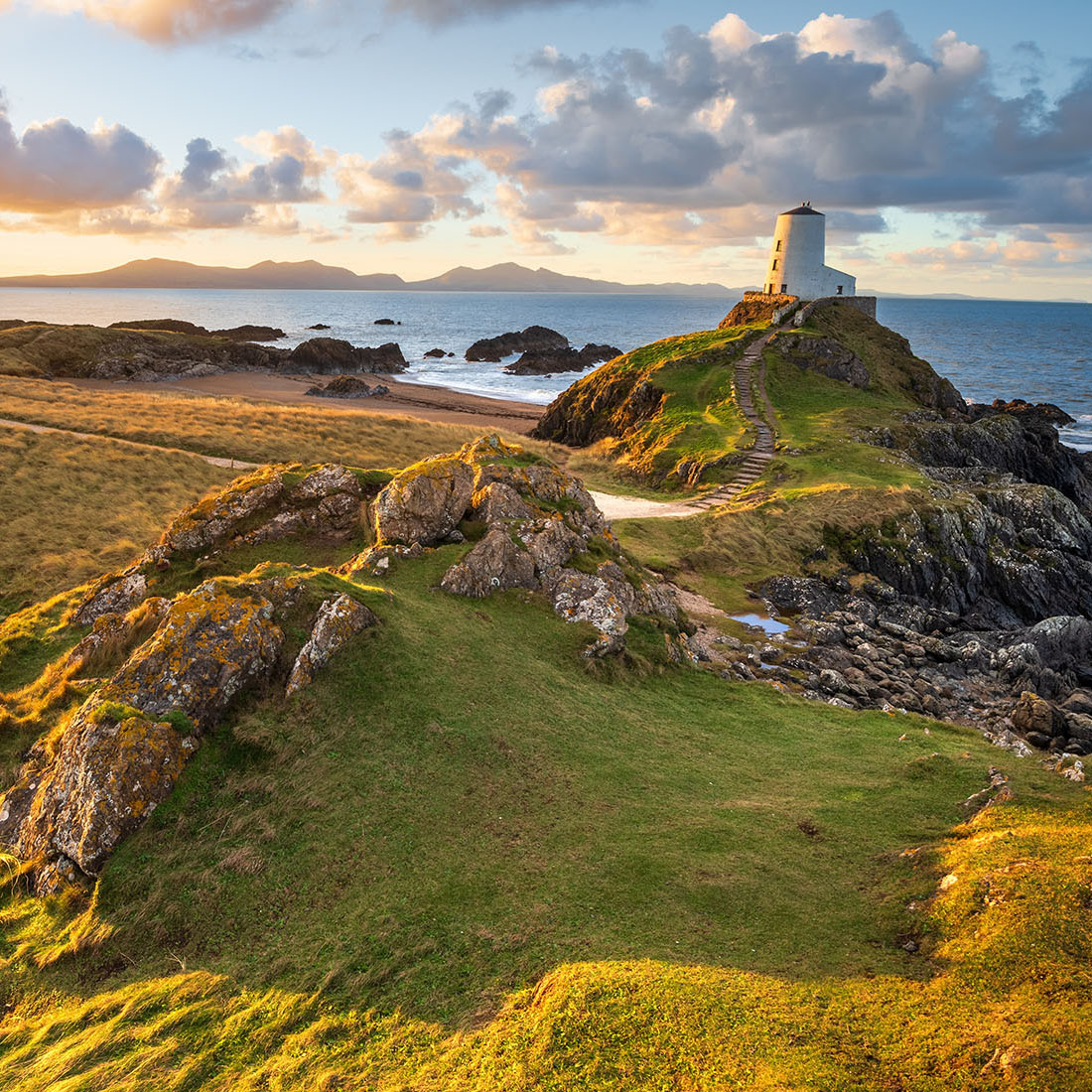 Rocky coastal landscape with grassy cliffs and a small stone tower by the sea at sunset