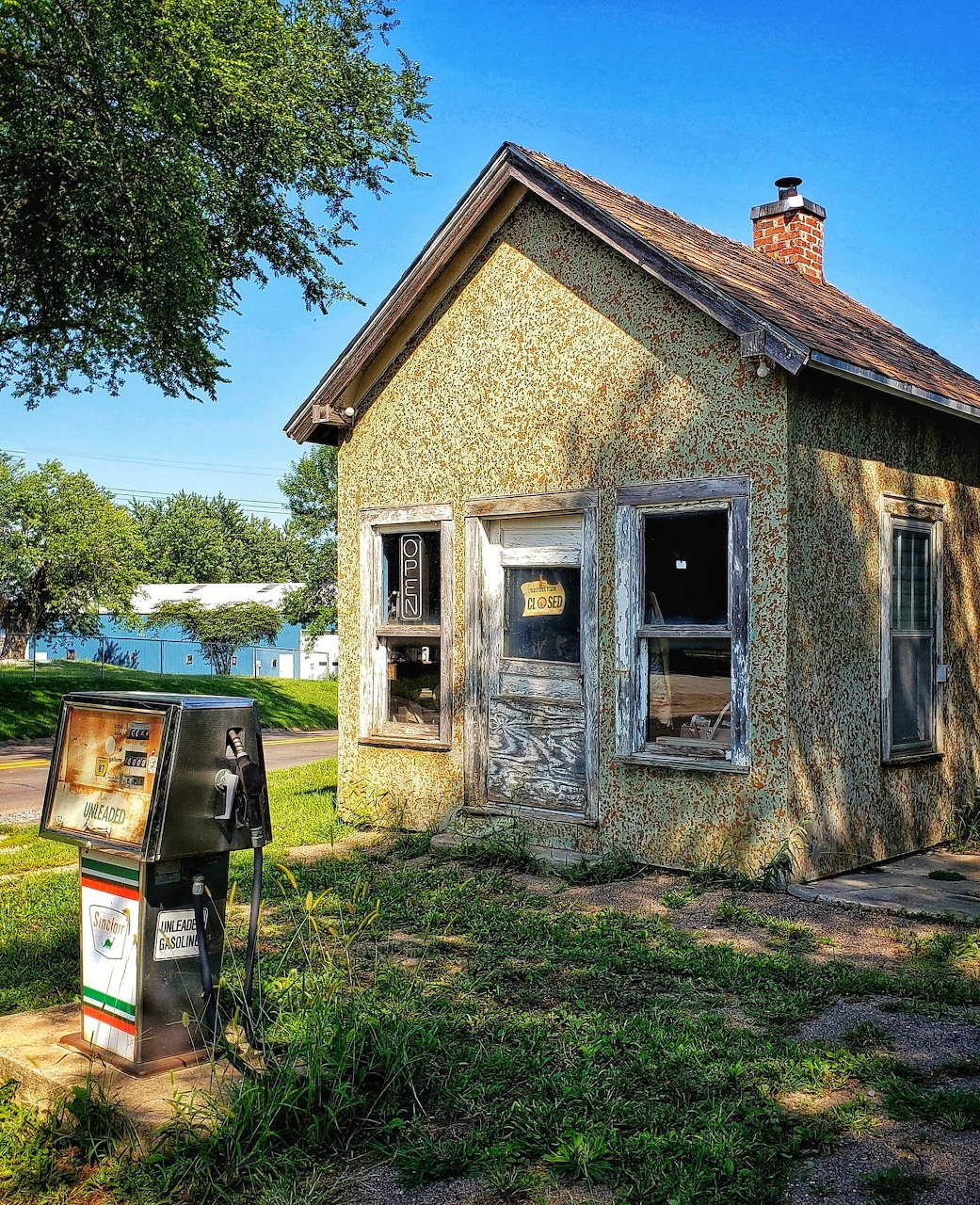 Old abandoned gas station building with vintage pump in overgrown rural setting by water